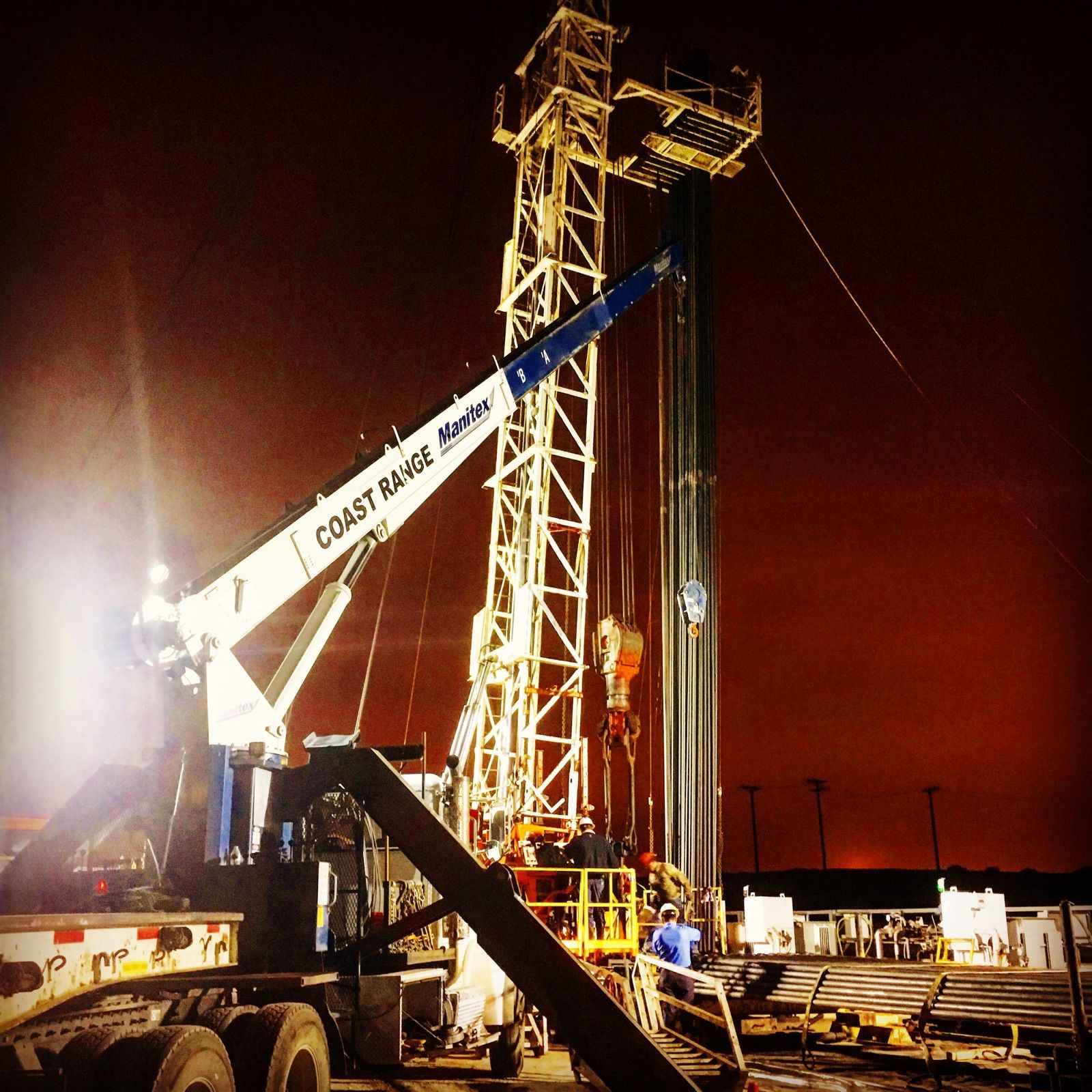A Coast Range Trucking crane working at an oilfield rig at sunset